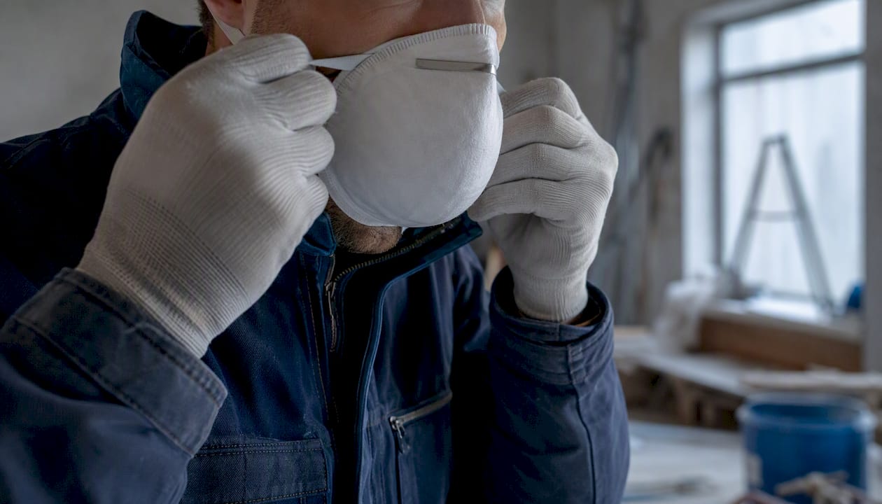 Des mains ajustent un masque de protection respiratoire contre l’amiante.