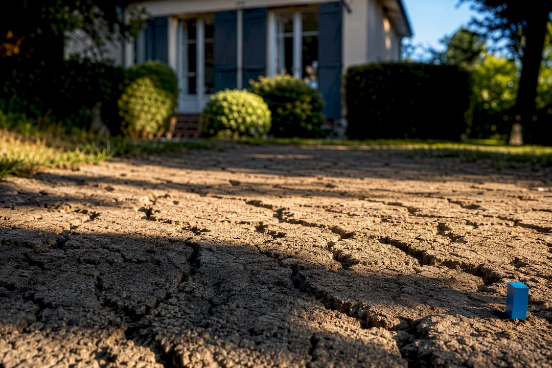 Terrain argileux craquelé devant une maison